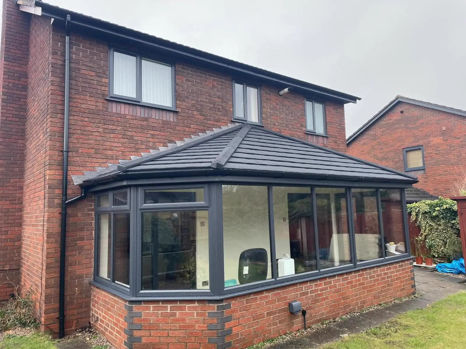 Dark-framed conservatory with a tiled roof and brick base