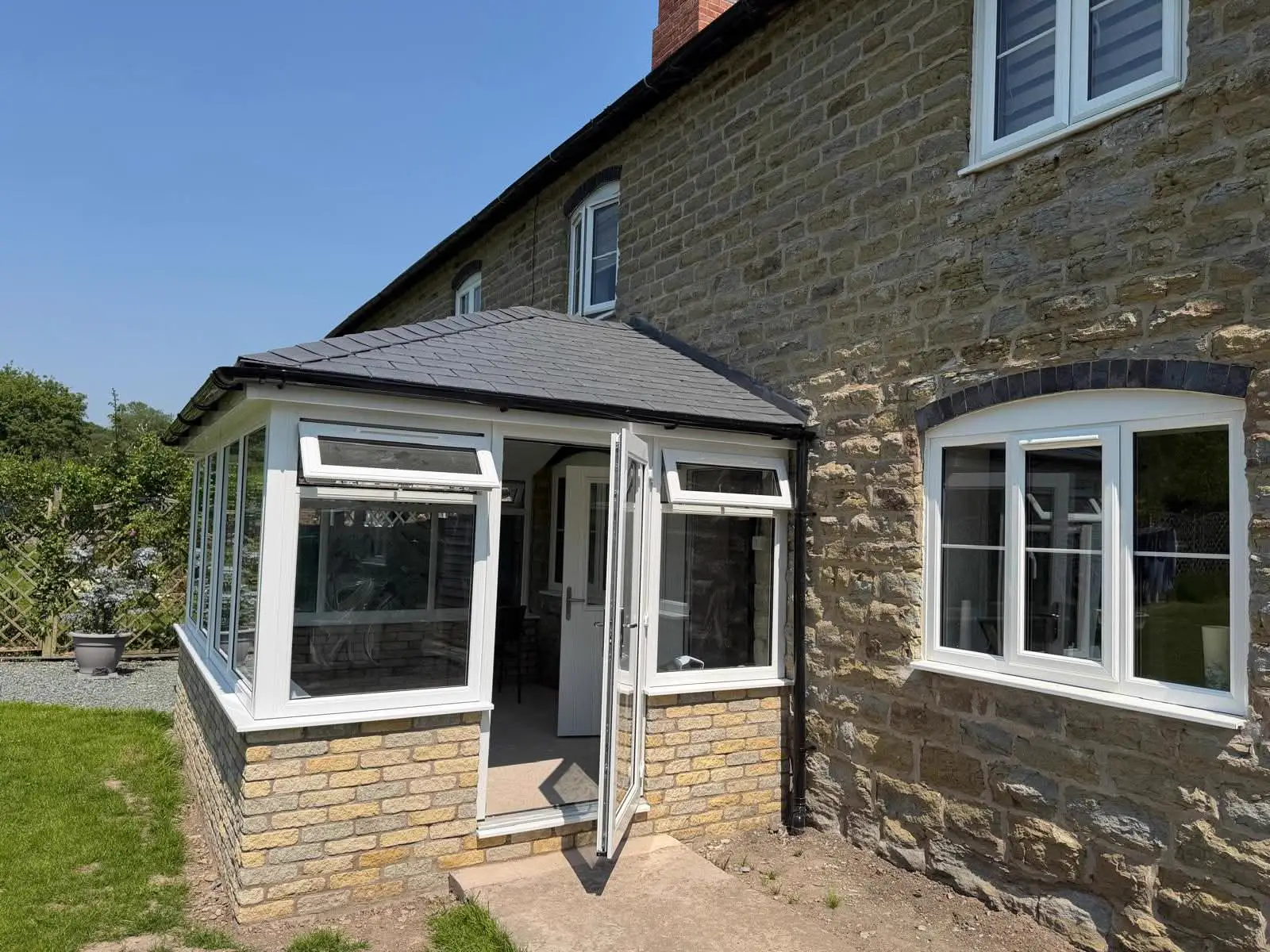 White-framed conservatory with a tiled roof beside a stone house